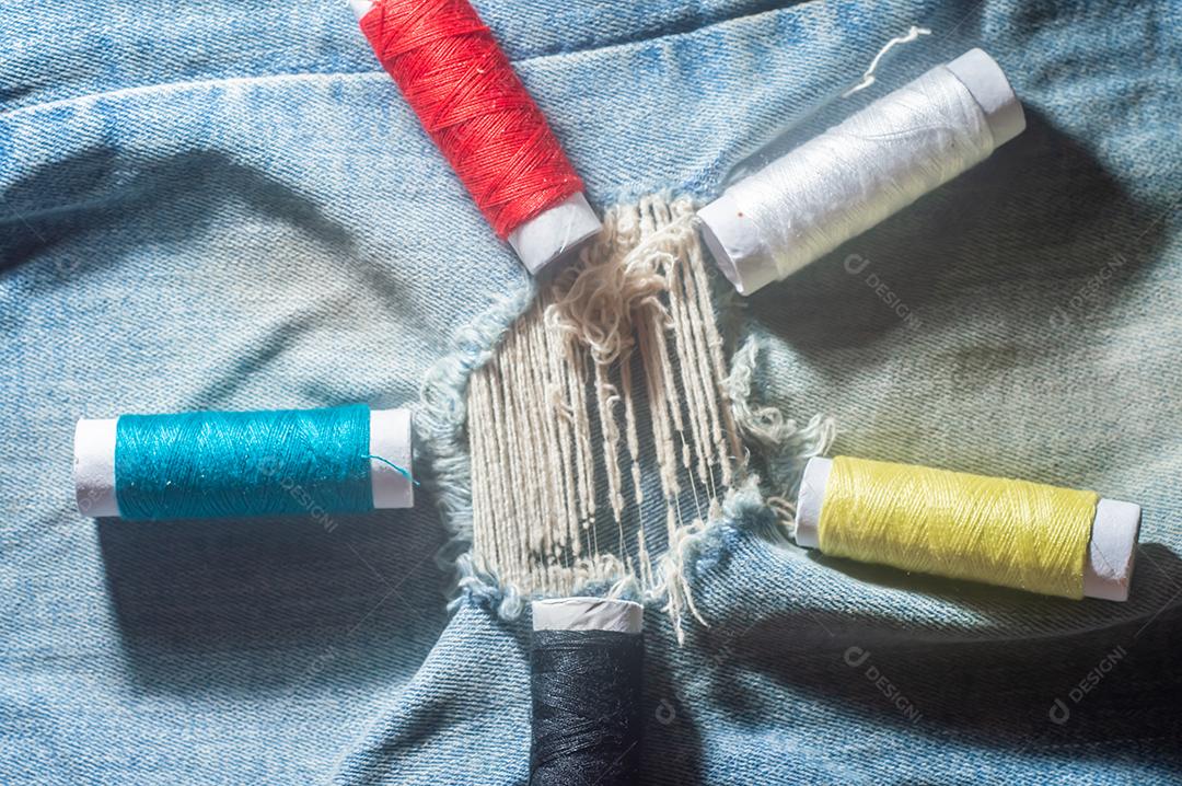 Bobinas com linhas de costura coloridas com jeans ao fundo, conceito de costura