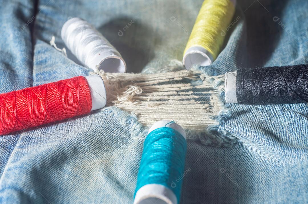 Bobinas com linhas de costura coloridas com jeans ao fundo, conceito de costura