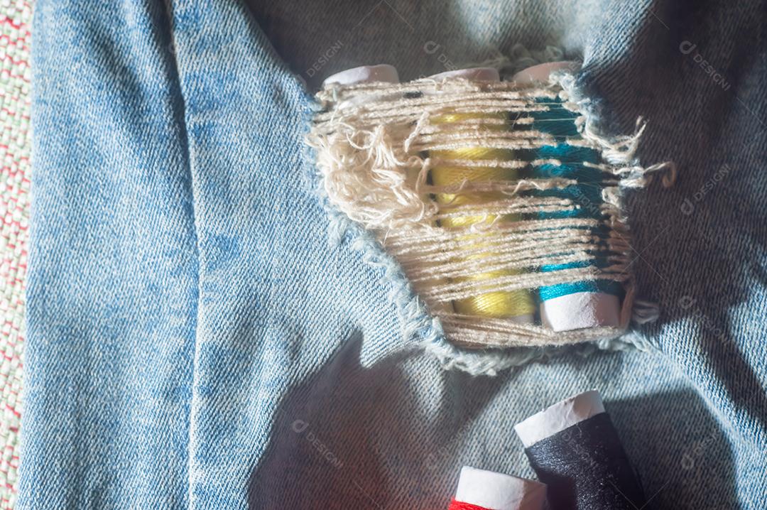 Bobinas com linhas de costura coloridas com jeans ao fundo, conceito de costura