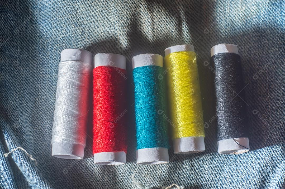 Bobinas com linhas de costura coloridas com jeans ao fundo, conceito de costura