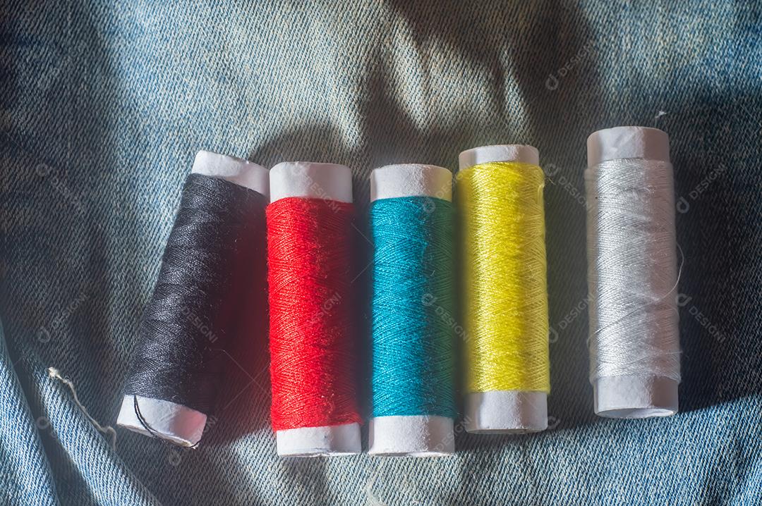 Bobinas com linhas de costura coloridas com jeans ao fundo, conceito de costura