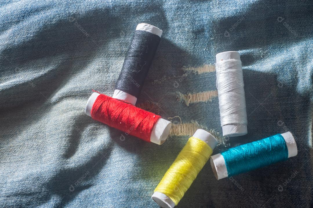 Bobinas com linhas de costura coloridas com jeans ao fundo, conceito de costura