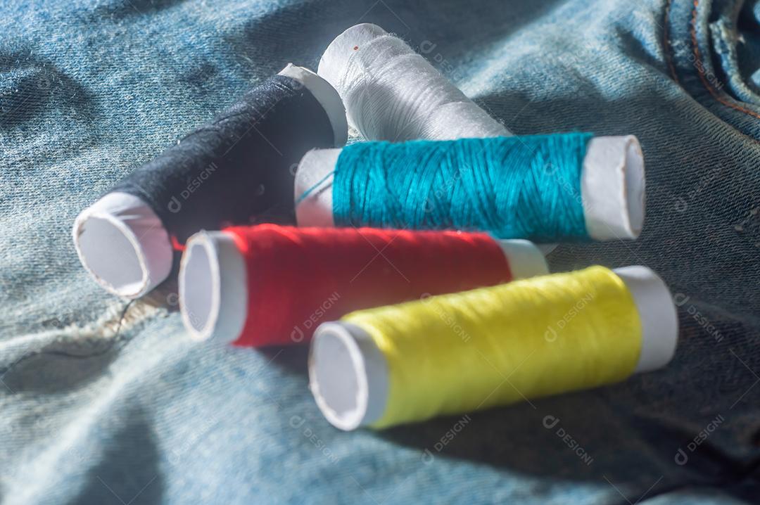 Bobinas com linhas de costura coloridas com jeans ao fundo, conceito de costura