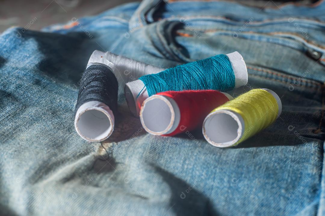 Bobinas com linhas de costura coloridas com jeans ao fundo, conceito de costura
