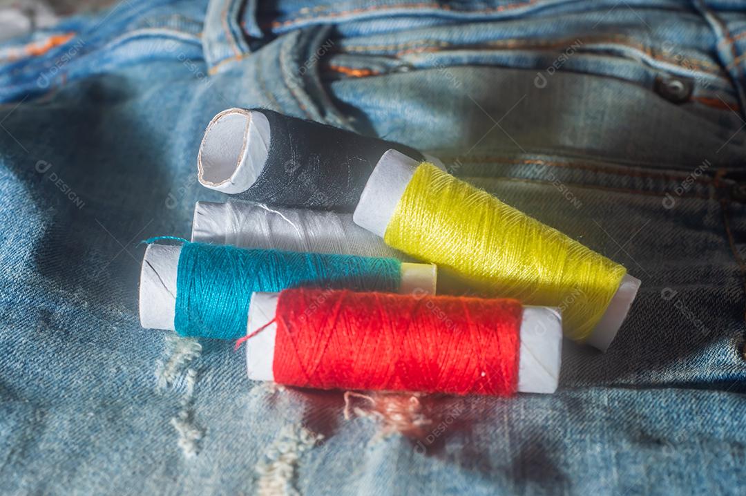 Bobinas com linhas de costura coloridas com jeans ao fundo, conceito de costura