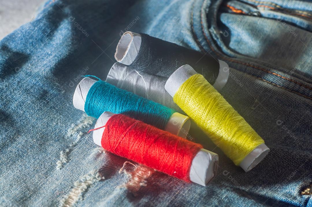 Bobinas com linhas de costura coloridas com jeans ao fundo, conceito de costura