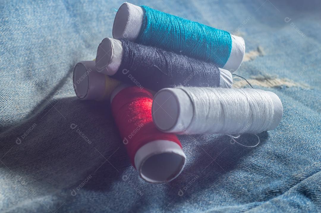 Bobinas com linhas de costura coloridas com jeans ao fundo, conceito de costura