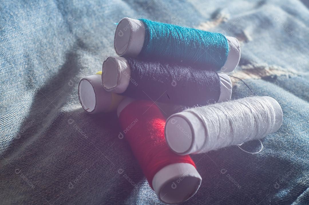 Bobinas com linhas de costura coloridas com jeans ao fundo, conceito de costura