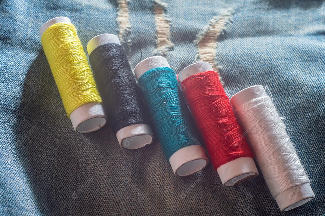 Bobinas com linhas de costura coloridas com jeans ao fundo, conceito de costura