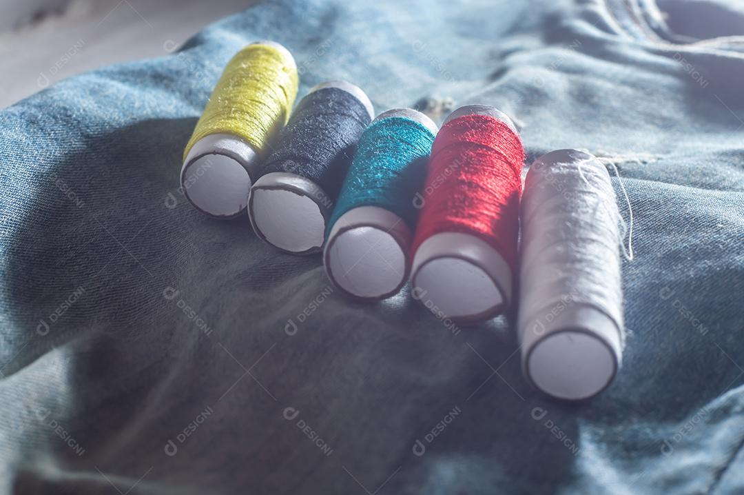 Bobinas com linhas de costura coloridas com jeans ao fundo, conceito de costura