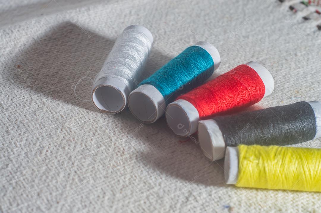 Bobinas com linhas de costura coloridas com toalha de mesa ao fundo, conceito de costura