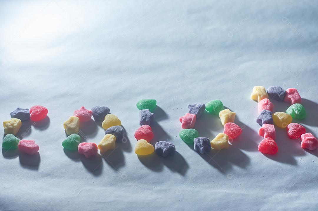 Doces coloridos variados com a palavra Cores escrita, fundo azul claro.