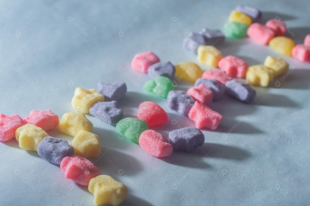 Doces coloridos variados com a palavra Cores escrita, fundo azul claro.