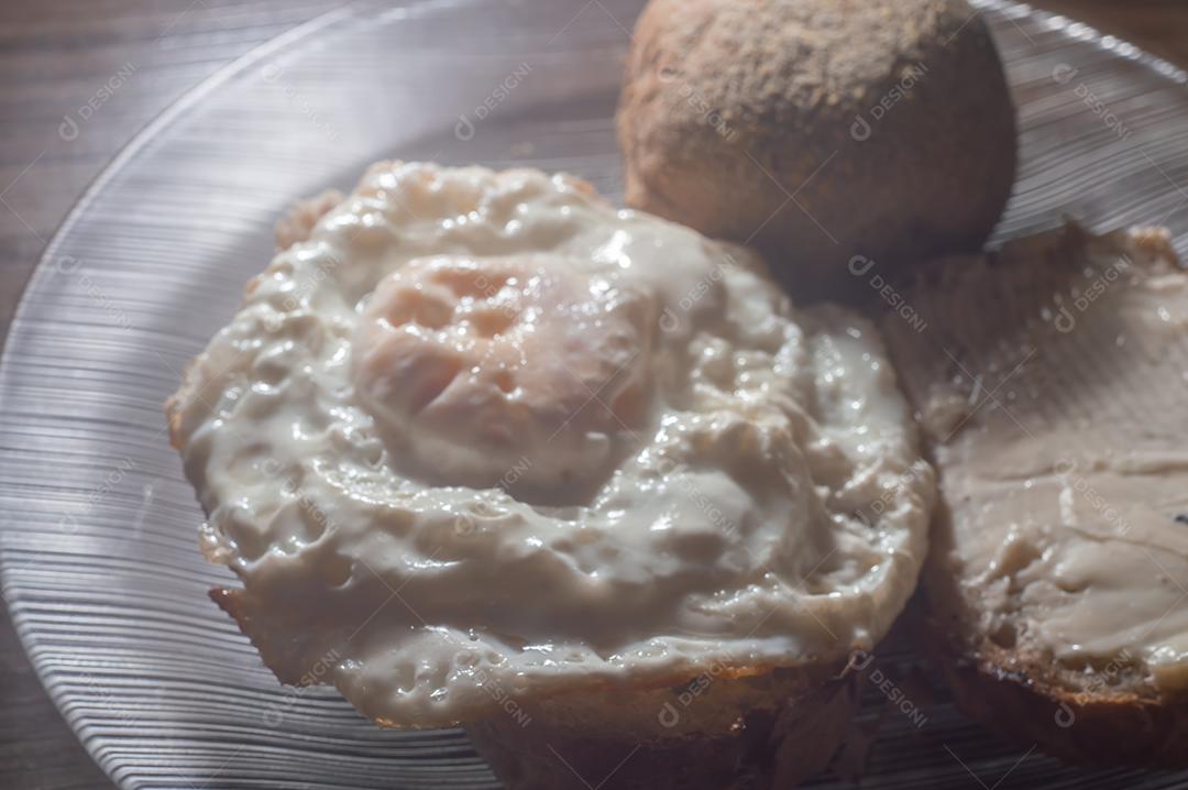 Pão artesanal com manteiga e ovo frito, em um prato transparente