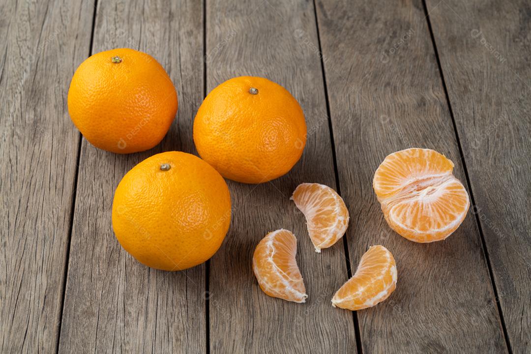 Tangerinas com frutas cortadas sobre a mesa de madeira