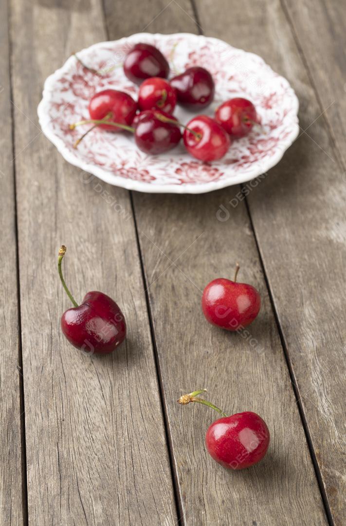 Cerejas vermelhas em um prato sobre a mesa de madeira
