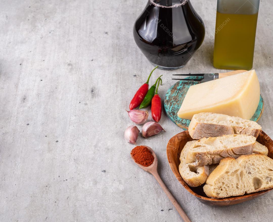 Pão, queijo parmesão, azeite, pimenta e alho sobre madeira
