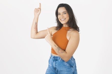 Mulher jovem usando blusa laranja usando suas mãos para apontar para cima sobre fundo branco