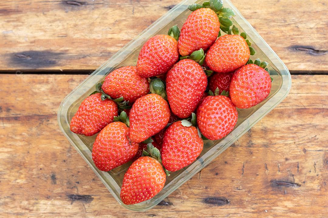 Forma cheia de morangos vermelho sobre mesa de madeira vista de cima