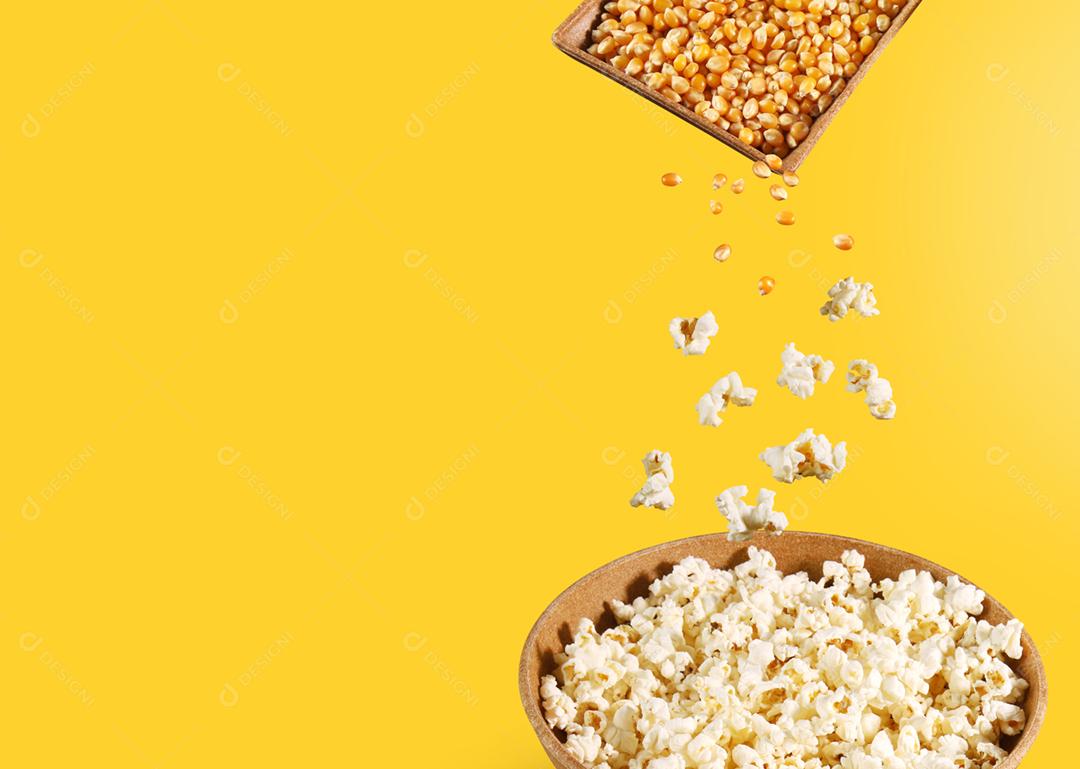 Milho e pipoca em movimento, caindo na tigela no backgrou amarelo