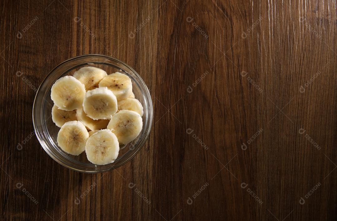 Bananas cortadas em uma tigela de vidro em uma mesa de madeira. Vista superior, copie sp