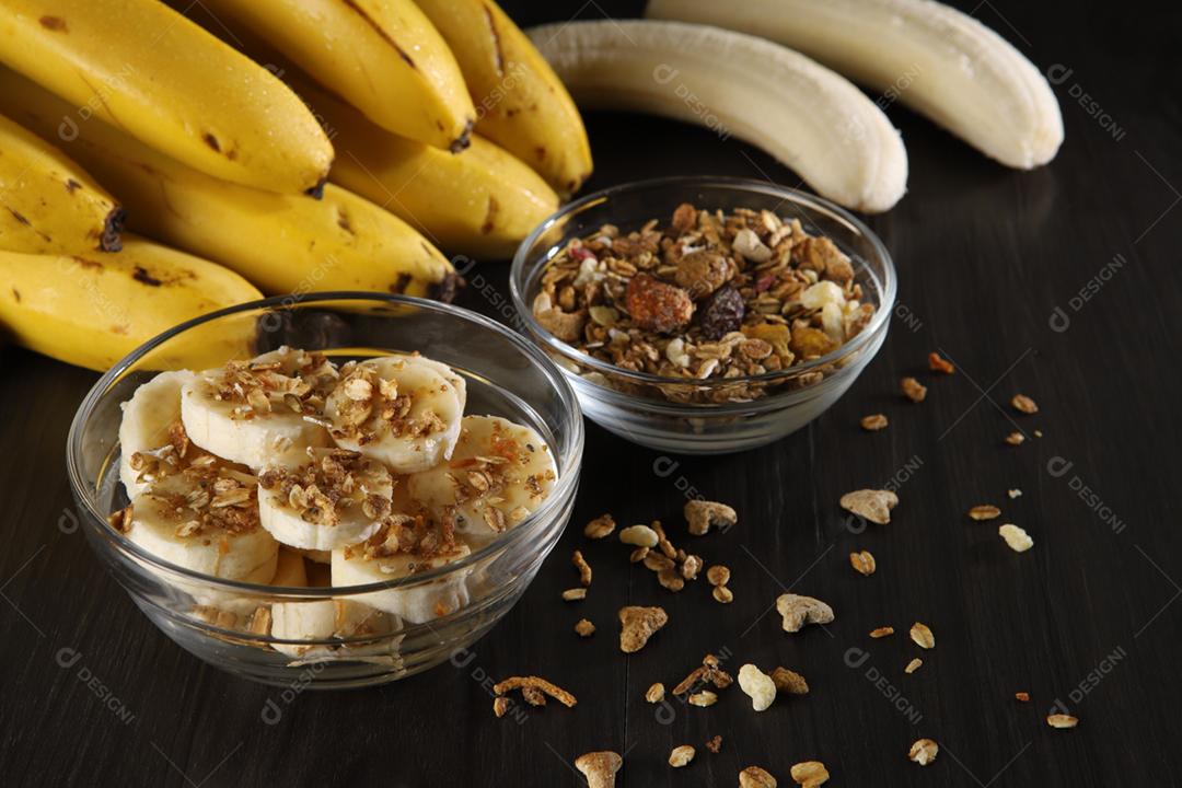 Um banquete de bananas com granola e cereais em madeira cinza escuro