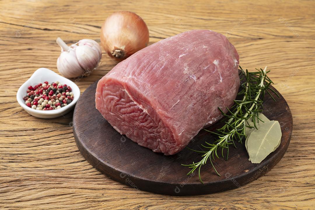 Carne redonda de olho cru sobre tábua de madeira com temperos.
