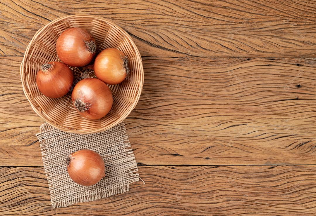 Cebolas em uma cesta sobre a mesa de madeira