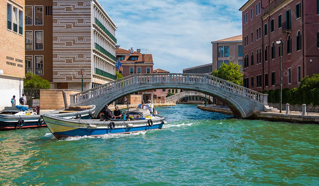 Vista do canal de Veneza com barco passando sob ponte histórica.