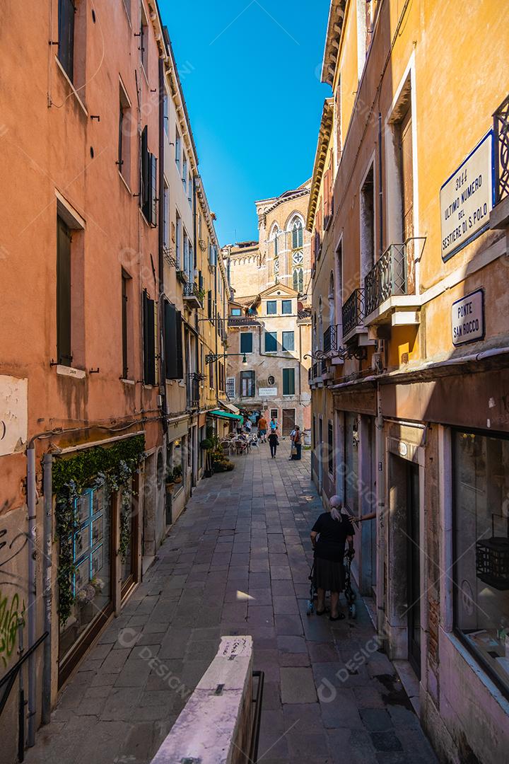 Vista de pessoas andando por casas históricas em um beco estreito em Veneza.