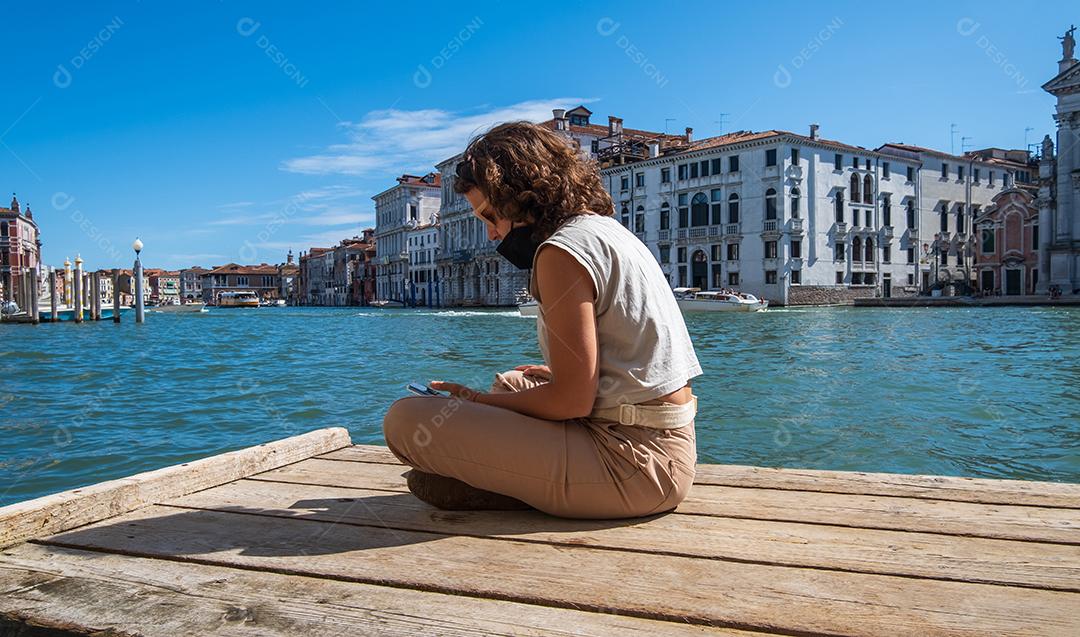 Jovem mulher usando telefone celular no cais de canais em Veneza, na Itália.