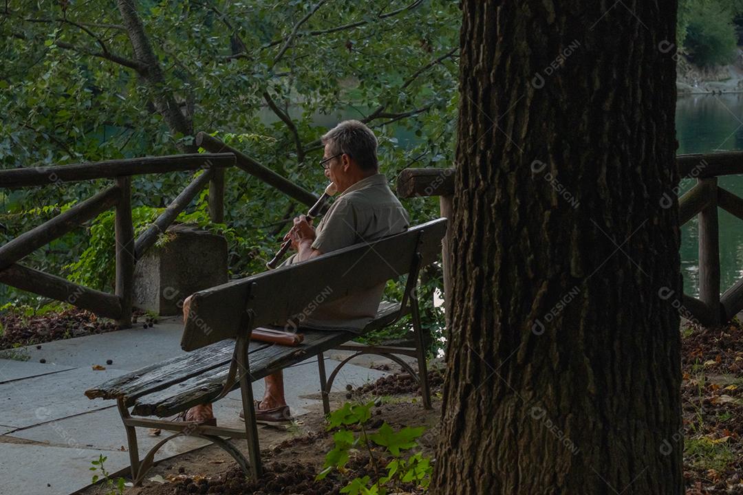 Um velho tocando flauta no parque.