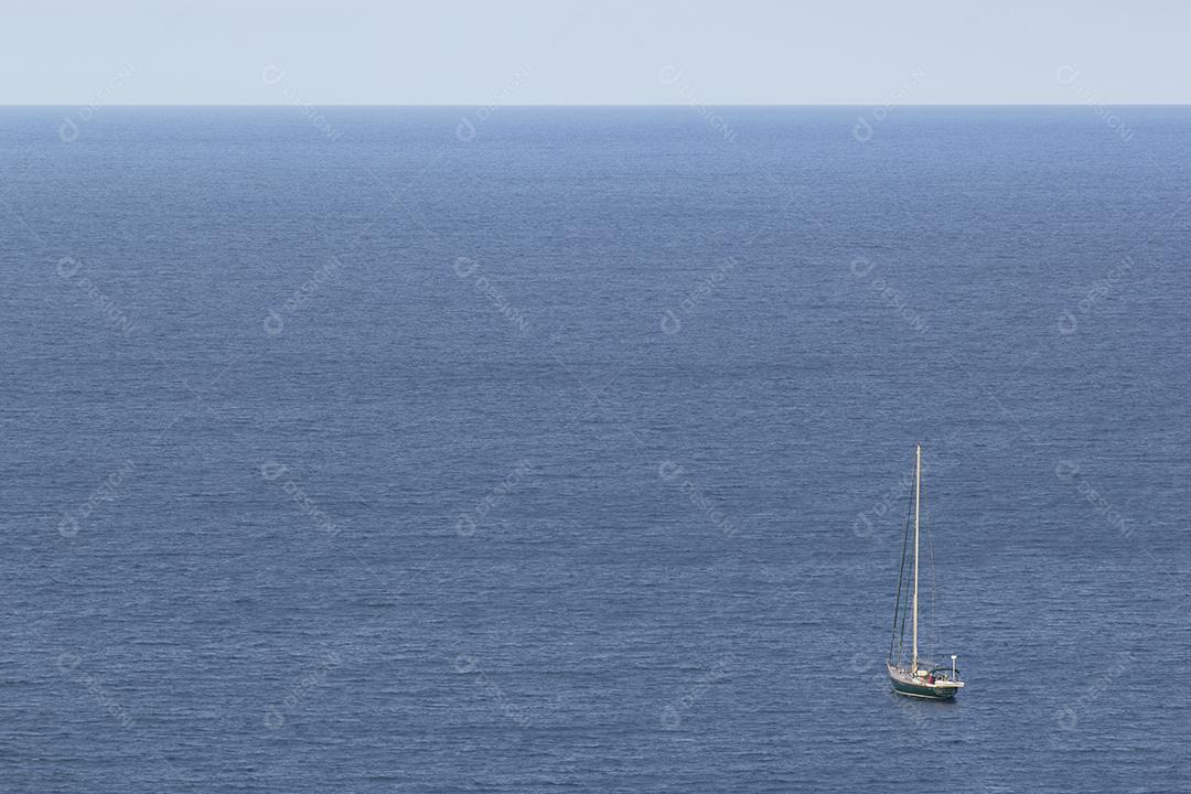 Barco à vela sobre um oceano azul calmo de frente para o horizonte.