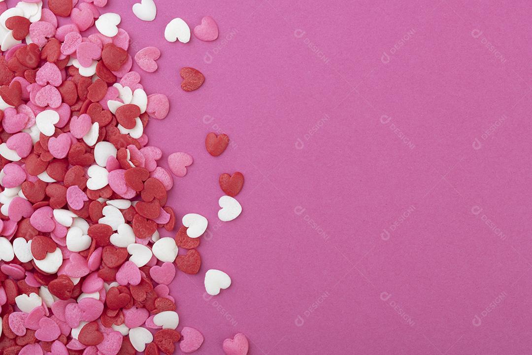 Um grupo de pequenos corações vermelhos, brancos e rosa sobre fundo rosa