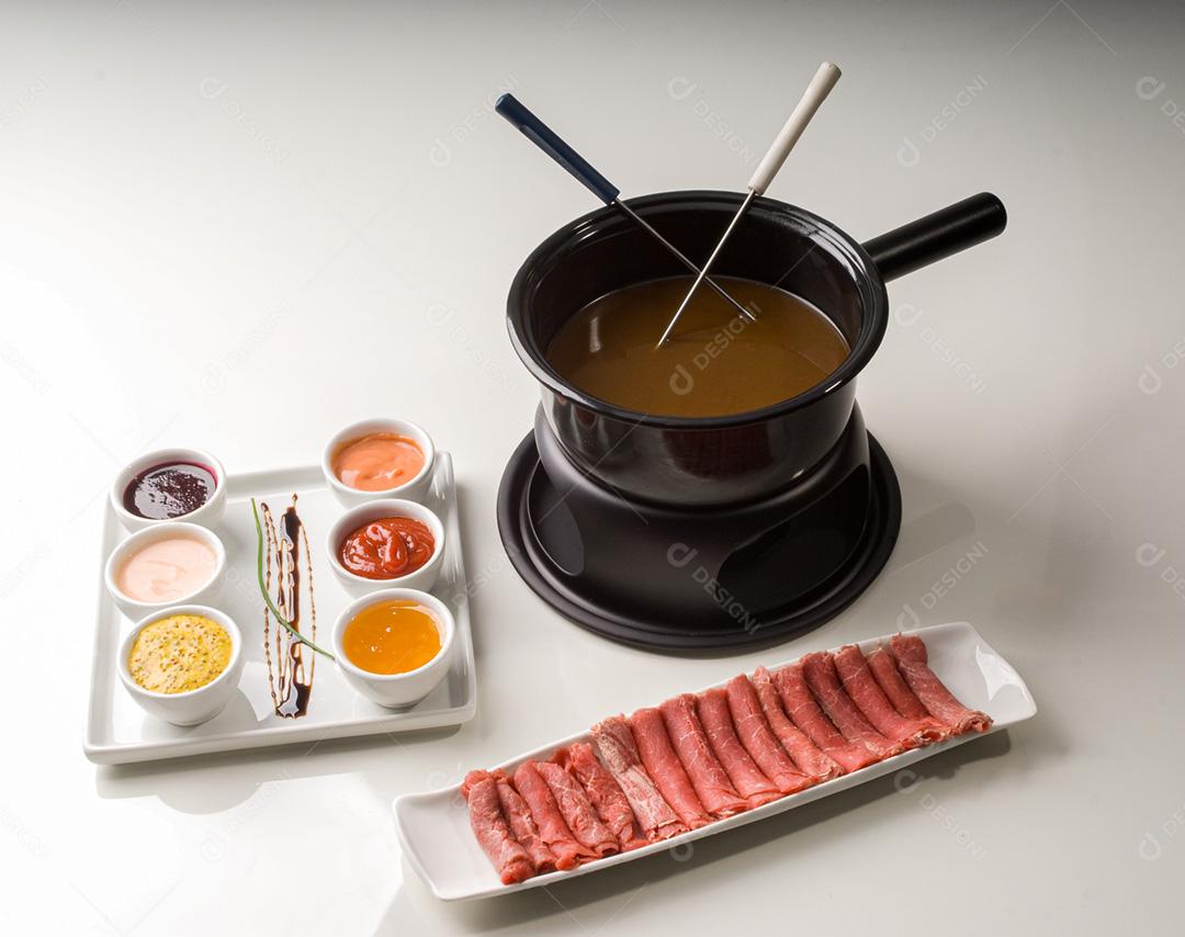 Fondue com petisqueira com molhos e bandeja de carnes em rolinhos