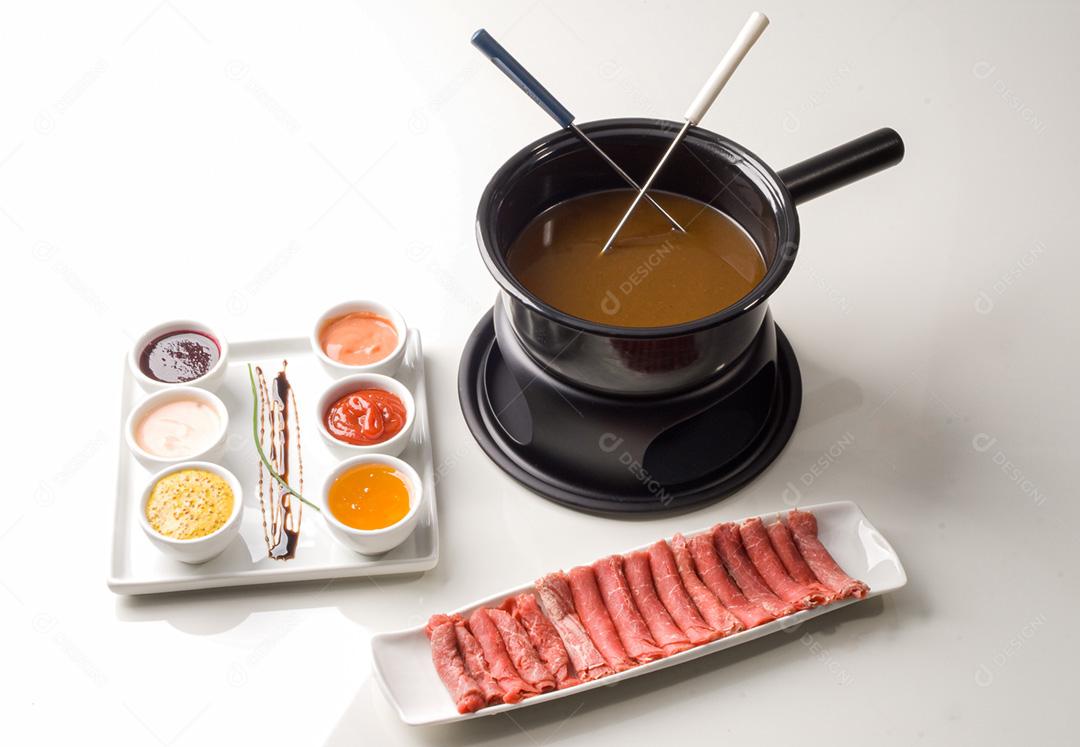 Fondue com petisqueira com molhos e bandeja de carnes em rolinhos