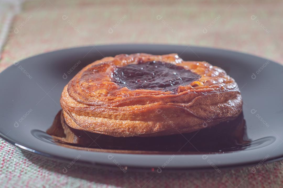 Massa folhada doce recheada com geleia de jabuticaba em prato preto com luz suave.