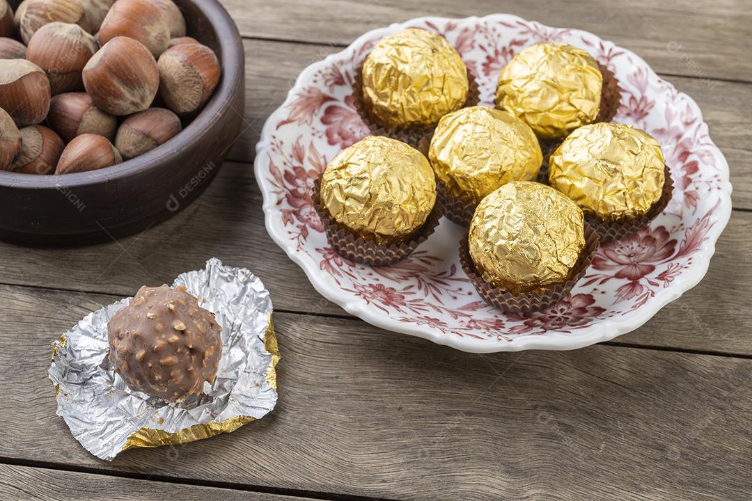 Chocolates recheados de avelã e avelãs sobre a mesa de madeira.