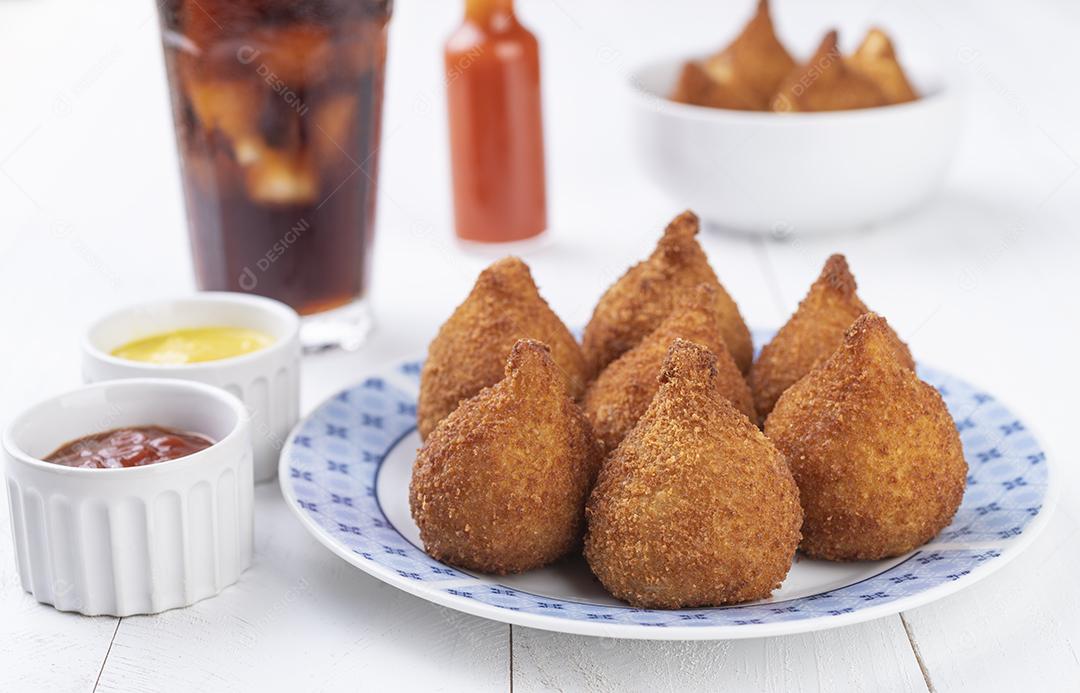 Coxinha de lanche típico brasileiro em um prato com copo de refrigerante.