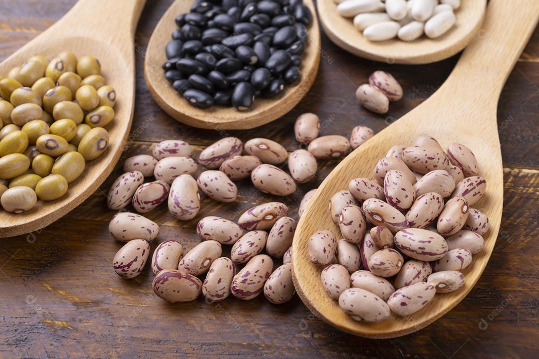 Feijão sortido em colheres sobre a mesa de madeira.