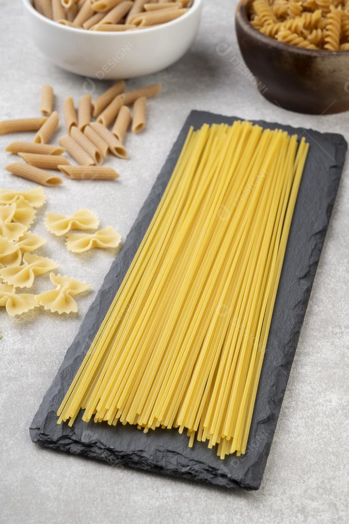 Macarrão espaguete, farfalle, fusilli e penne sobre bancada de concreto.