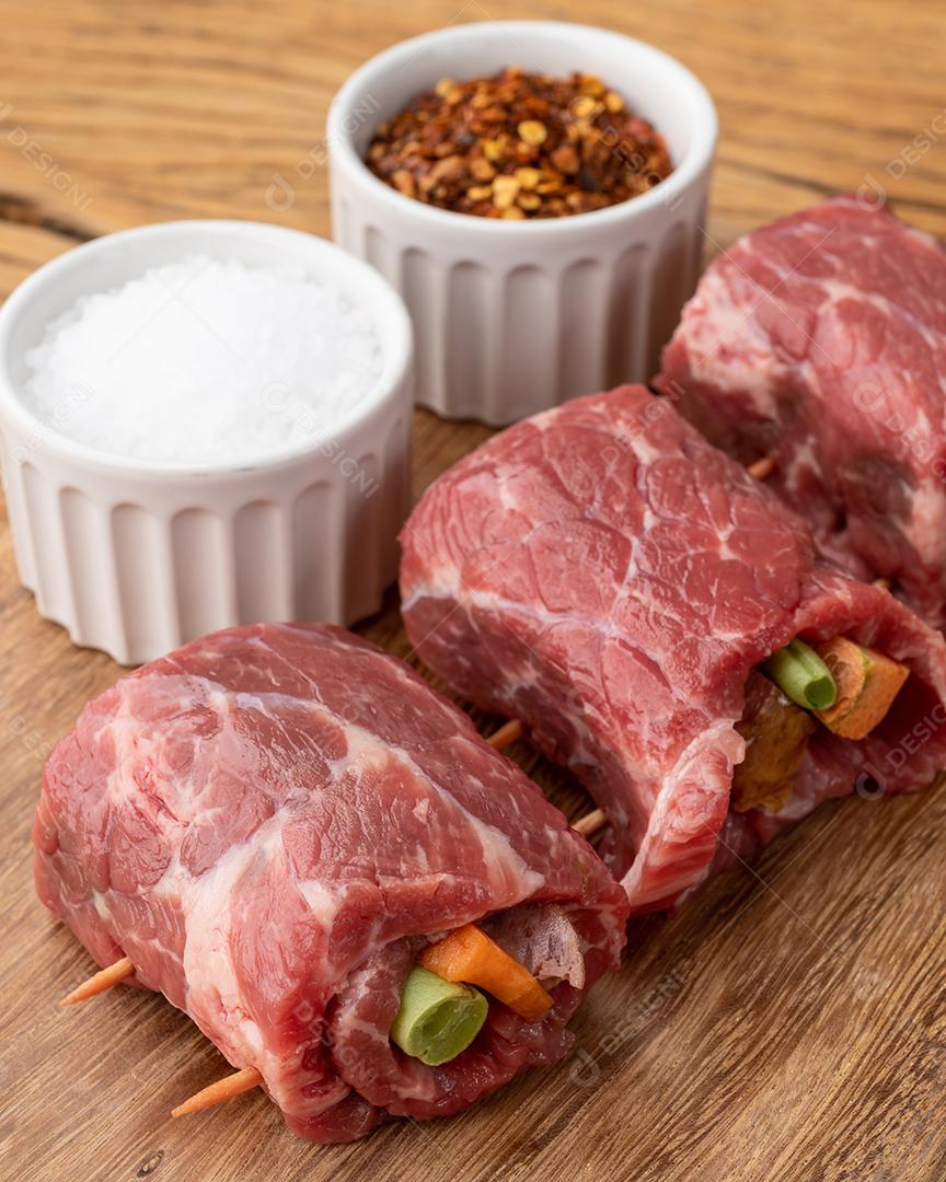 Enrolado de carne ou rocambole, legumes e bacon recheado de carne sobre mesa de madeira com temperos.