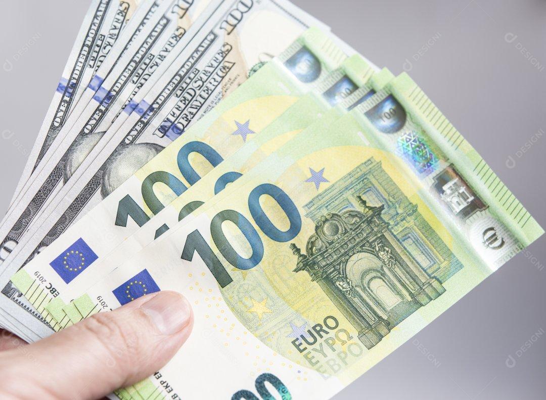 Mão segurando várias notas de dolar e euro