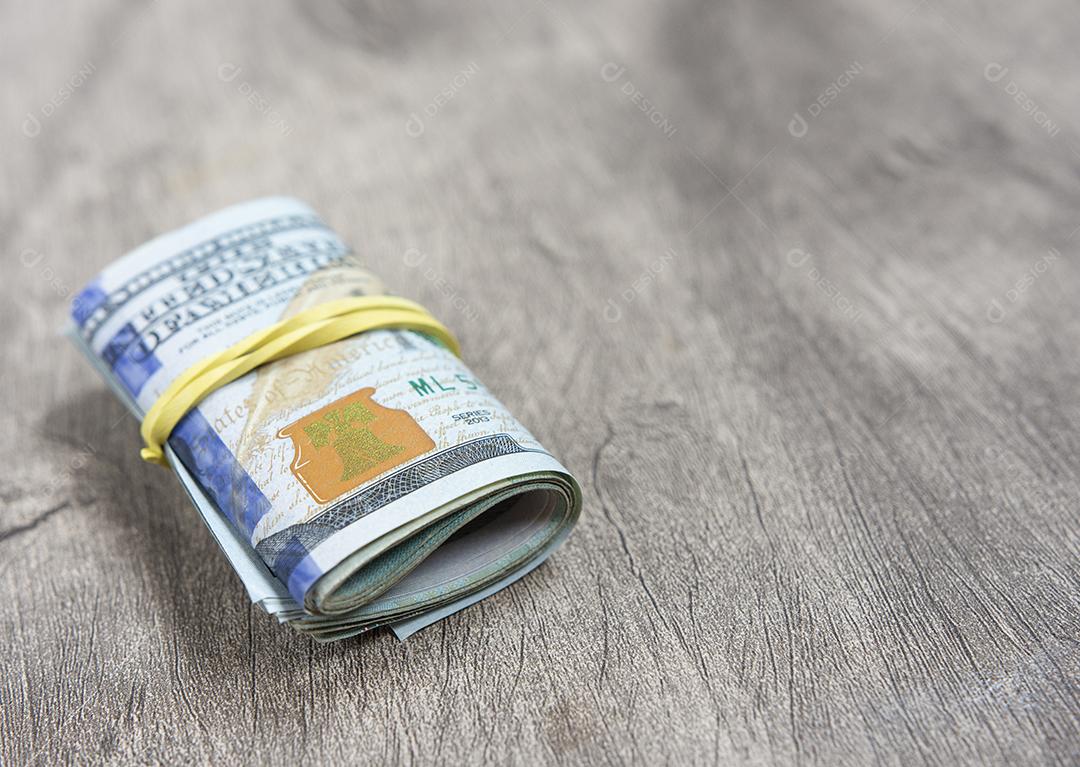 Notas de cem dólares embaladas em um elástico sobre fundo de madeira.