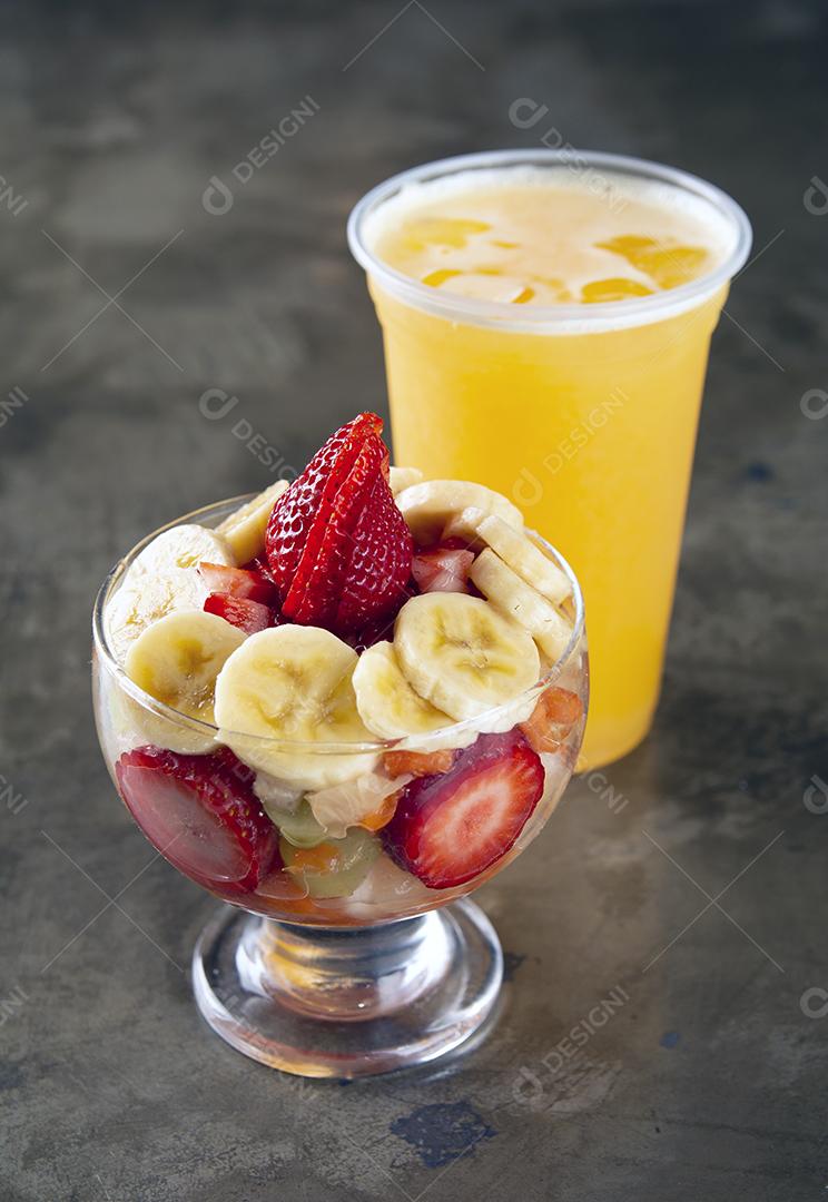 Salada de frutas em um copo com suco de laranja sobre fundo de pedra.