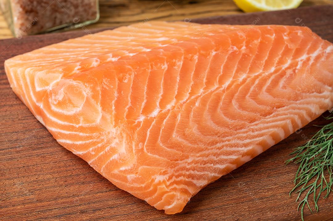 Filé de salmão cru com endro sobre placa de madeira.