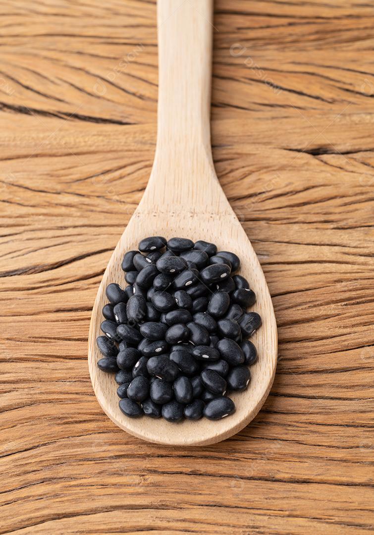 Feijão preto em uma colher sobre a mesa de madeira.
