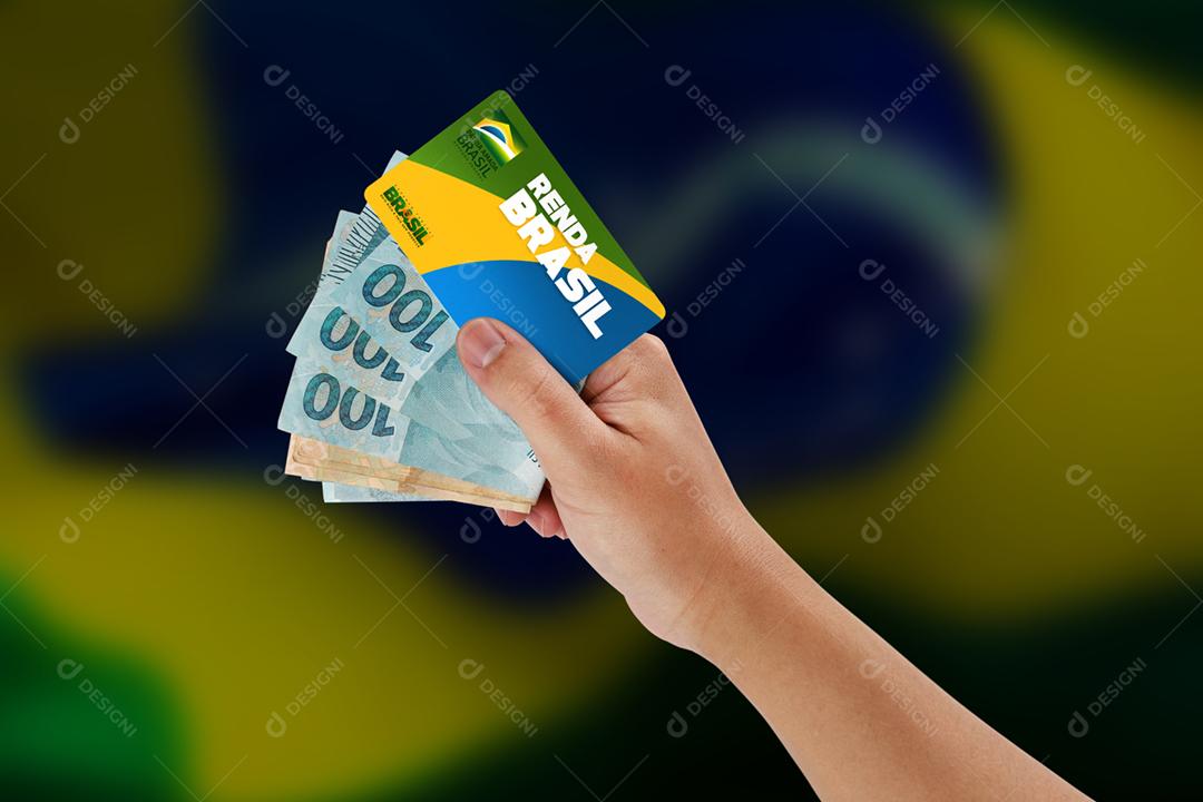 Curitiba, Paraná, Brasil, 06 de setembro de 2020. Mão brasileira segurando cartão e dinheiro do novo programa de ajuda popular chamado Renda Brasil. Novo auxílio emergencial e bolsa família. Fundo da bandeira.