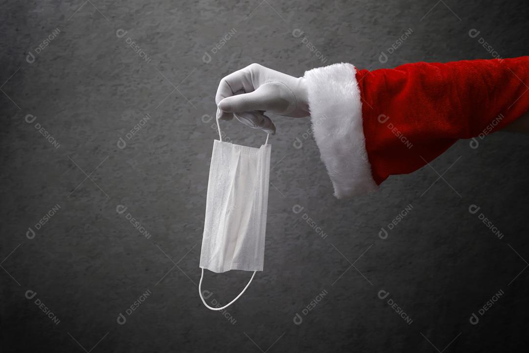 mão com luva de Papai Noel em pandemia segurando ma protetora