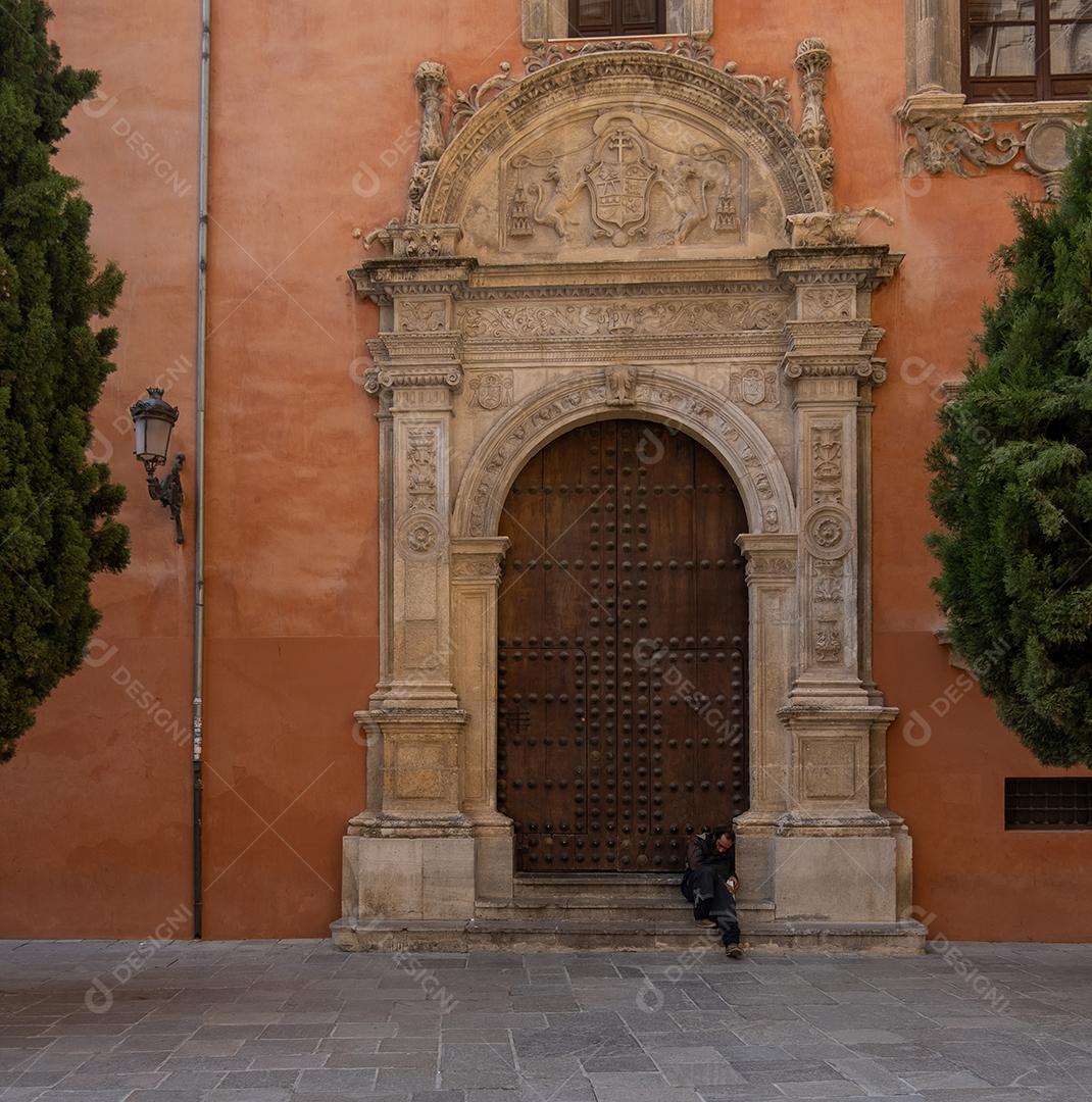 Sem-teto sentado na porta medieval de uma igreja em Granada.